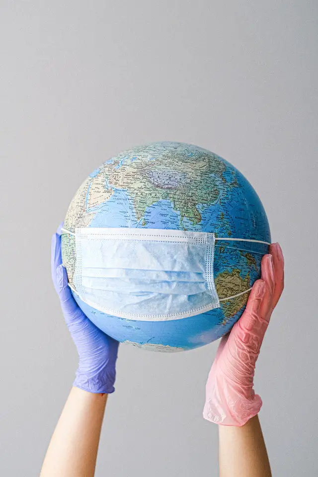 the globe or world wearing a mask held up by human hands